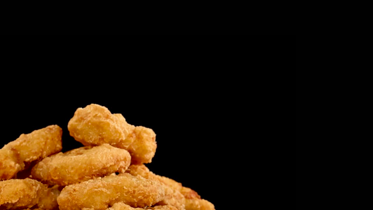 Golden, crumbed chicken nuggets rotate in slow motion against a black background, highlighting crispy texture and spicy seasoning with dramatic studio lighting