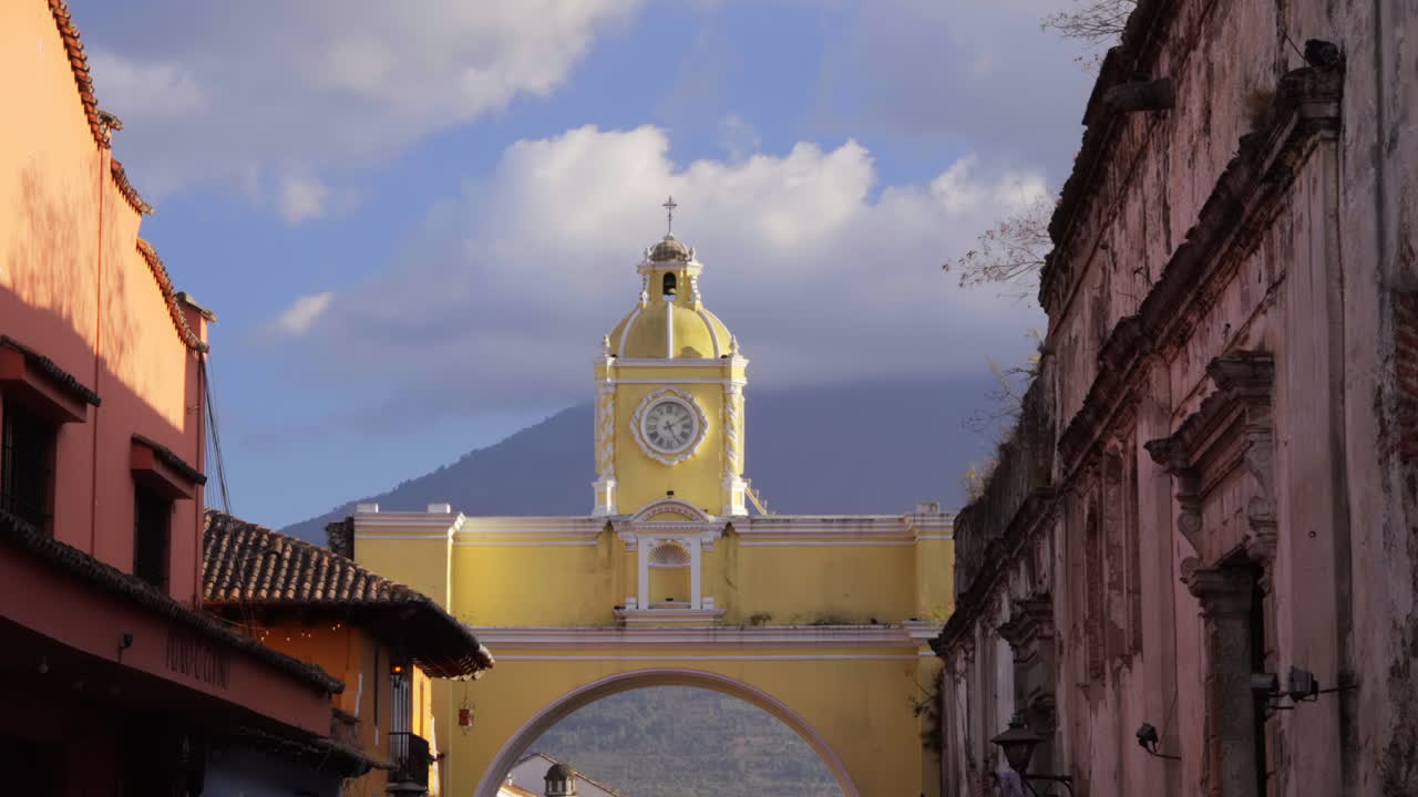 Historic Santa Catalina Arch stretches over cobblestone street with volcano backdrop, bird flies in slow motion, tilt down