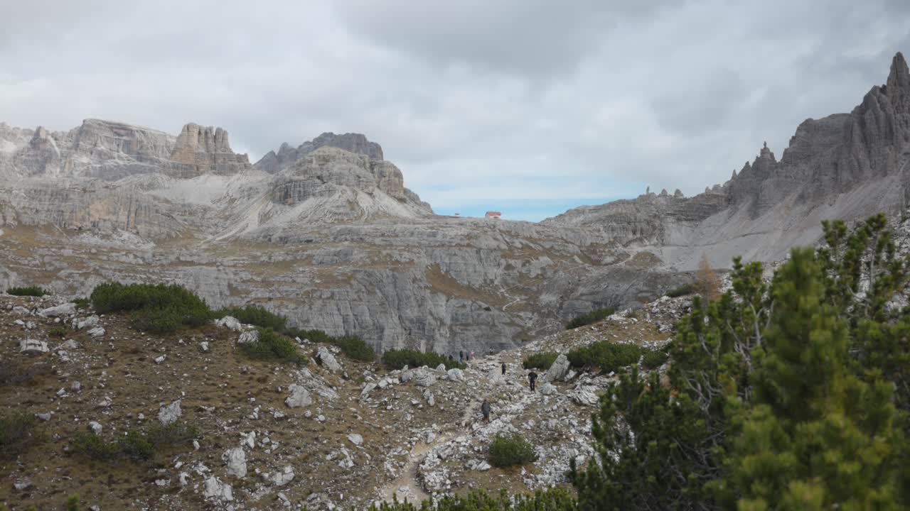 A stunning panning shot of Veneto's 3 Cime Lavaredo, with clouds floating above and hikers visible in the background