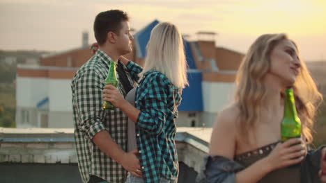 two young couples dancing with their halves on the roof. they enjoy time with beer.