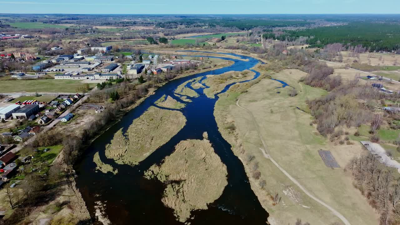 Drone captures Venta flowing past town, through flat fields, early Baltic spring