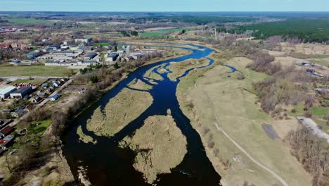 drone captures venta flowing past town, through flat fields, early baltic spring