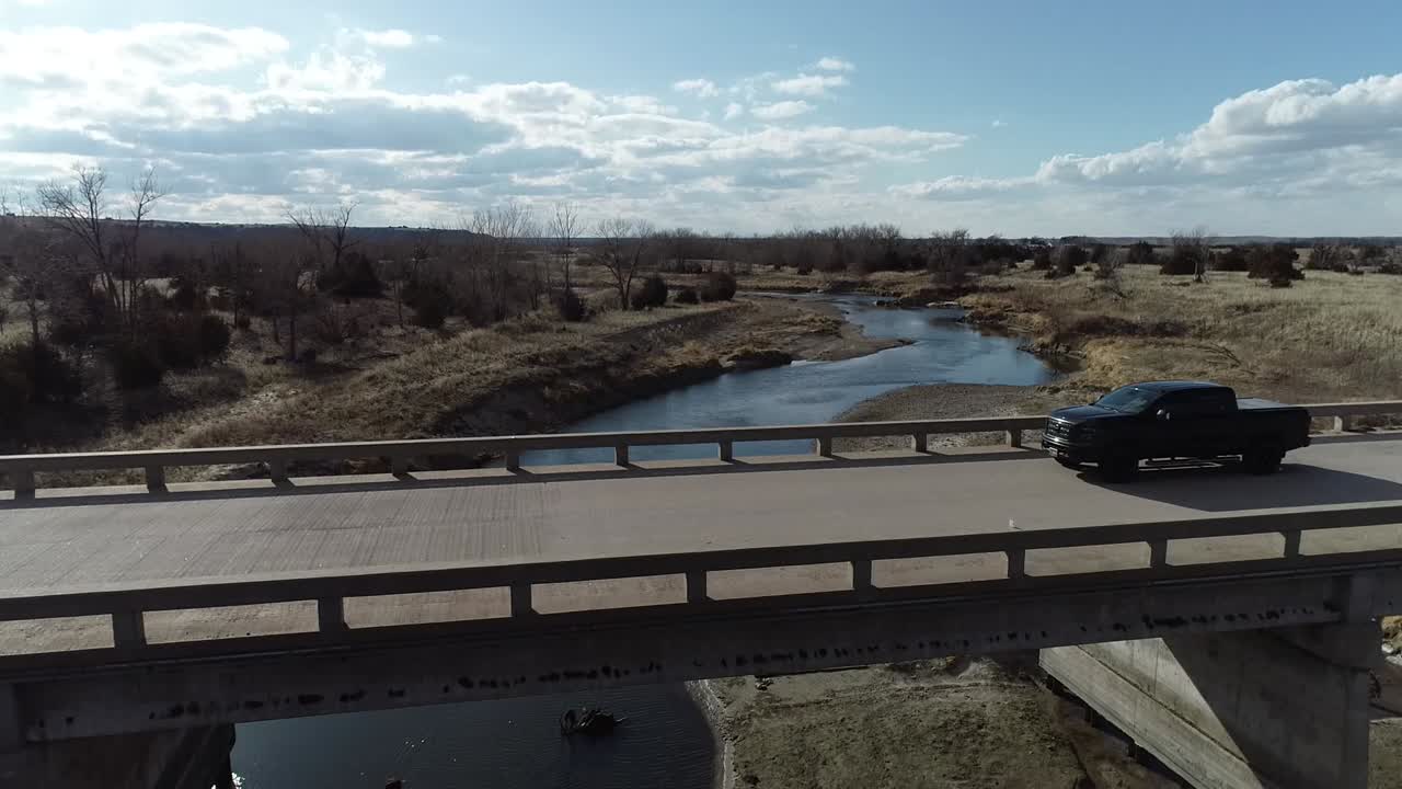 Rising aerial of a black pickup truck crossing a concrete bridge in the midwest