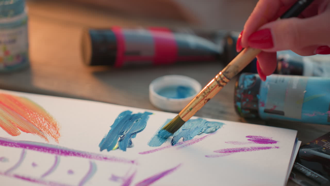 mature woman using brush to apply vibrant color strokes on white paper sheet, hands close showing textured paint layers blending multiple hues for artistic creation in outdoor garden setting