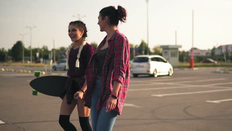 vista lateral de dos jóvenes hipsters felices caminando juntas en el estacionamiento, hablando y riendo