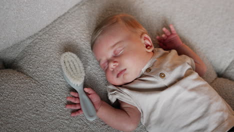 lovely caucasian newborn sleeping tight holding hands up. little baby having a hairbrush in his hand. close up.