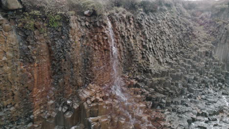 Aerial-parallax-around-small-waterfall-flowing-down-basalt-cliff-Studlagil-Canyon,-Iceland