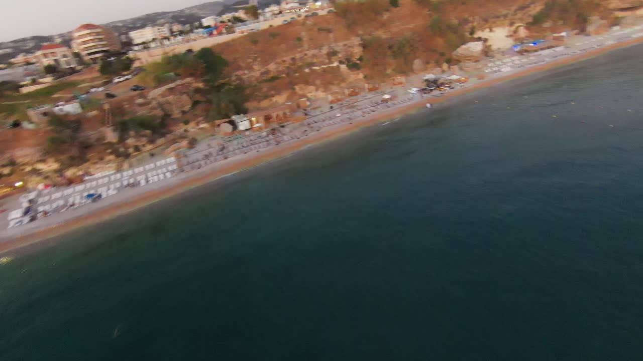 vuelo de drones de fpv a lo largo de una playa de arena con un hotel turístico en batroun, líbano al atardecer
