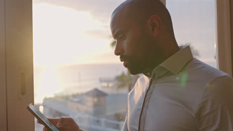 Un-Hombre-Atractivo-Usando-Un-Teléfono-Inteligente-En-Una-Habitación-De-Hotel-Al-Atardecer-Enviando-Mensajes-De-Texto-Revisando-Mensajes-Mirando-Por-La-Ventana-Planificando-Con-Anticipación