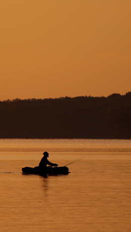silhouette of fisherman in boat. fishing on a lake from the boat at sunset vertical video