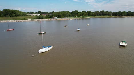 Drone-low-flight-over-moored-sailboats-calm-river-sunny-day,-left-to-right-gentle-twist-around-boats