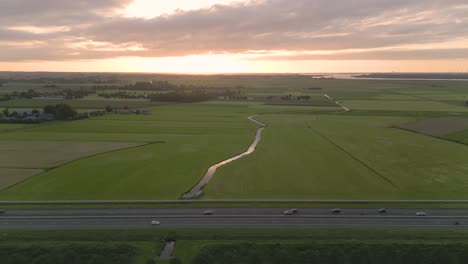 Drone-shot-of-the-highway-with-a-traffic-and-green-fields-at-sunset