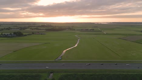 drone shot of the highway with a traffic and green fields at sunset