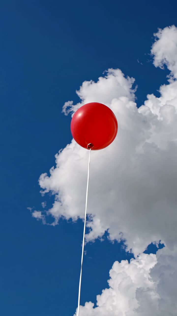 Upward angle captures a red balloon against a vivid blue sky with fluffy clouds