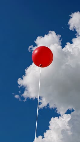 upward angle captures a red balloon against a vivid blue sky with fluffy clouds