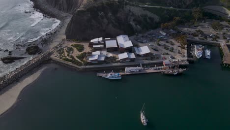 Aerial-pan-over-sea-cliffs,-calm-harbor-water,-and-crowded-dock