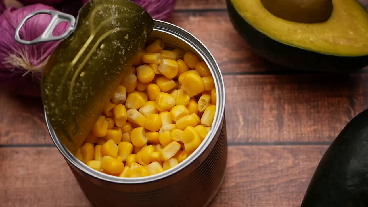 Canned corn, onions, and avocado on a wooden table
