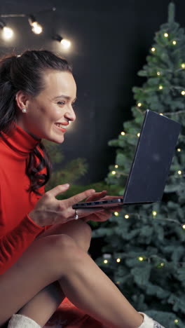 woman with laptop during christmas. young beautiful happy female using laptop on bed near christmas tree