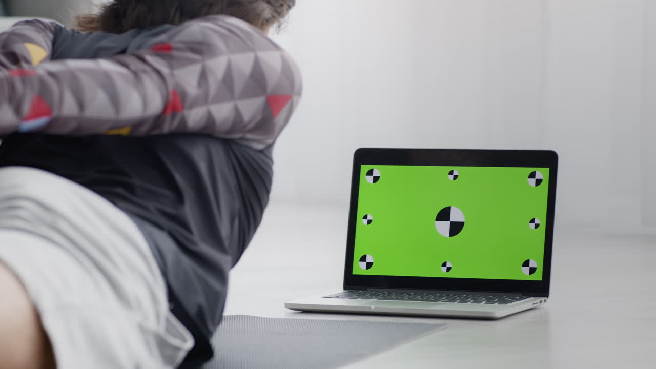 persona haciendo ejercicios de estiramiento frente a una computadora portátil con una pantalla verde