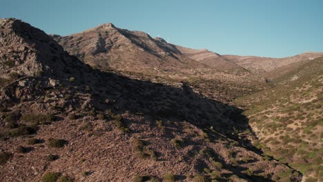 Panoramic-aerial-rising-overview-of-dry-shrubland-on-greek-island-of-syros,-mountainscape-sprawling