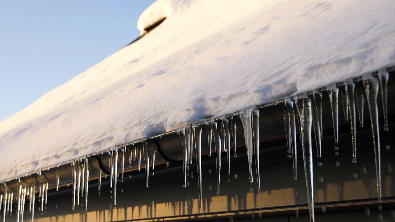 A serene winter landscape featuring a snow-covered roof with icicles hanging from a metal structure. The scene is captured in a wide angle shot, showcasing the calm and peaceful atmosphere.