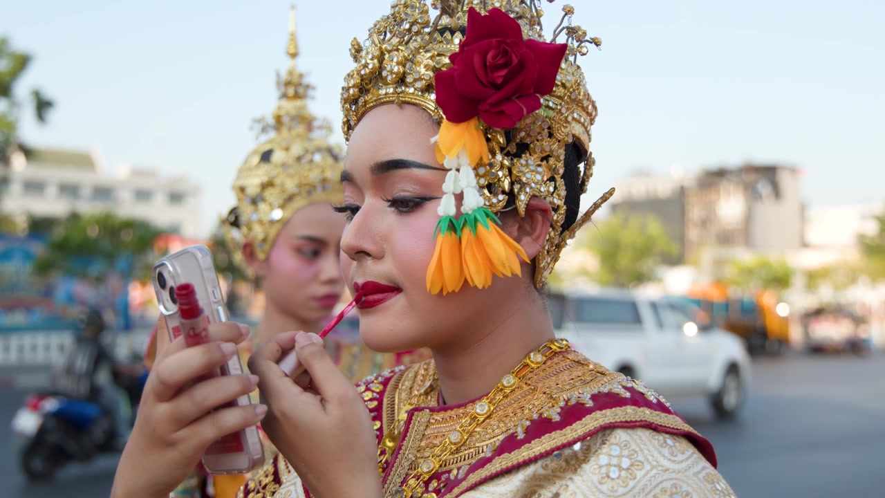 Một vũ công cổ điển Thái Lan thoa son môi đỏ bằng điện thoại thông minh làm gương ngoài trời.
