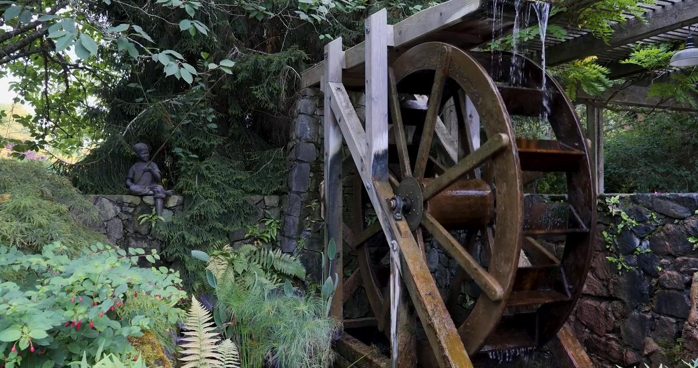 Kincir air yang terletak di Butchart Gardens di Victoria, British Columbia, Kanada. Kincir air kayu pedesaan berlatar dinding batu yang dikelilingi oleh tanaman hijau subur