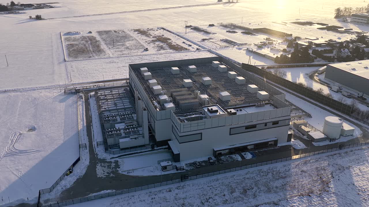 Orbiting aerial shot showcasing a large, modern data center building surrounded by snow covered fields during a cold winter day at sunset