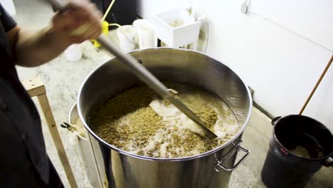 person stirring grain in pot of alcoholic beer at brewery