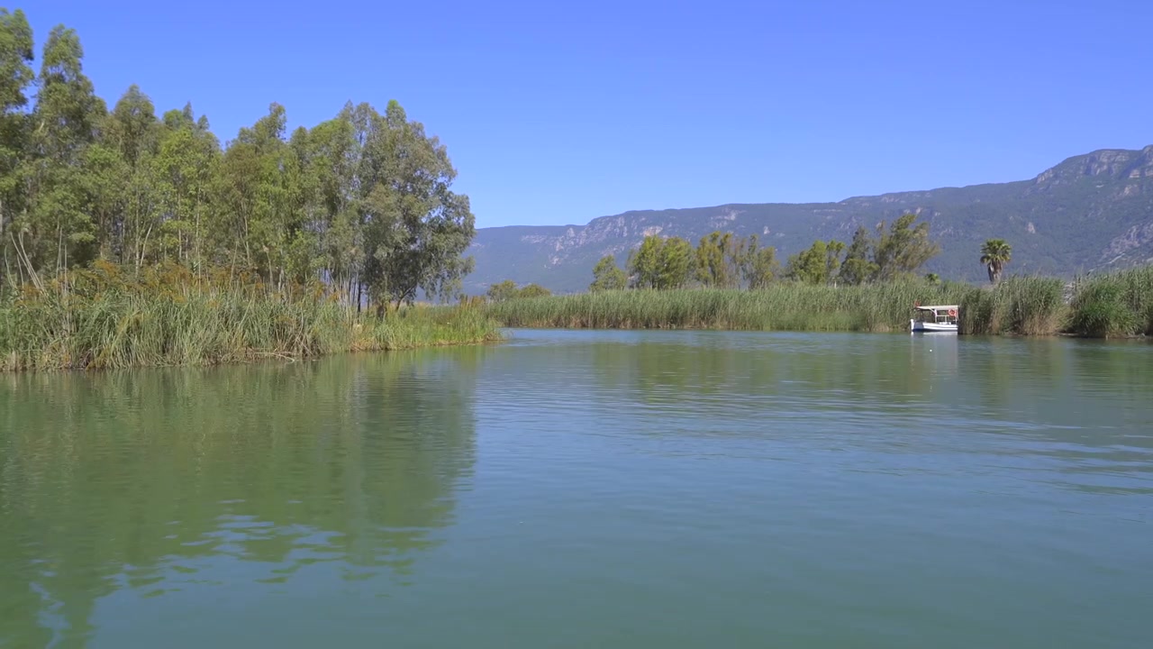 Piccola barca che naviga su un fiume calmo circondata da canne e montagne
