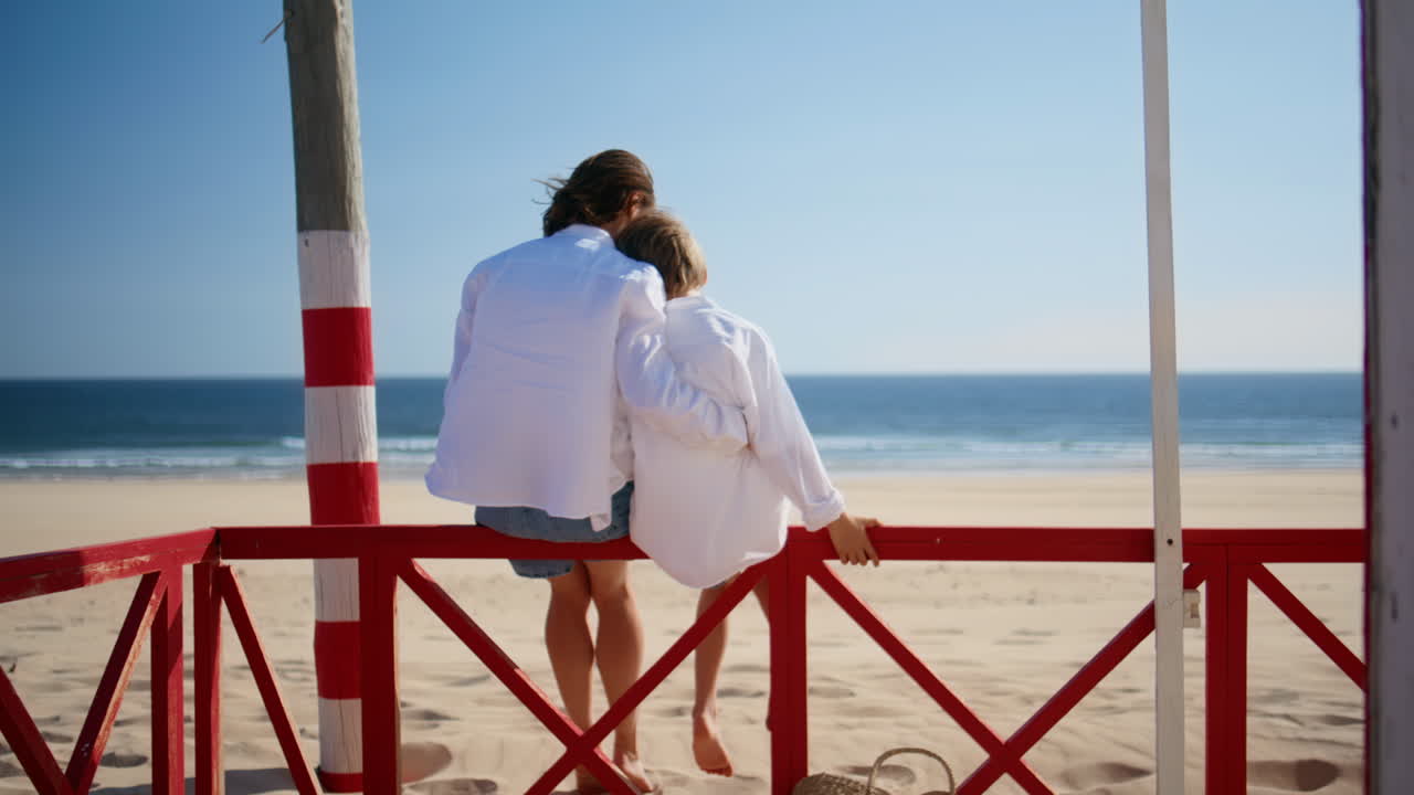 Woman son sitting fence beach overlooking ocean waves. Serene mother