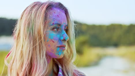 portrait of the blonde young and beautiful woman looking straight to the camera and smiling cheerfully while being in colorful spots of paints outside