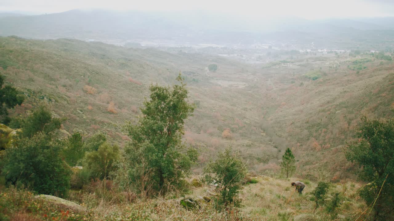 aldeano primitivo haciendo cosecha manual en la ladera sobre un amplio valle, tiro estático