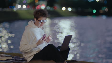 young woman using laptop in park and taking pictures of night city