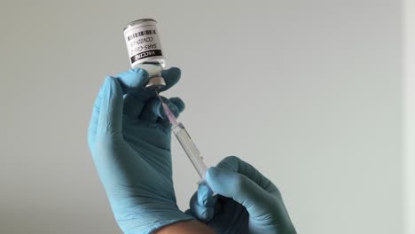 primer plano de las manos de la enfermera con guantes quirúrgicos, sosteniendo una jeringa succionando la vacuna para covid-19