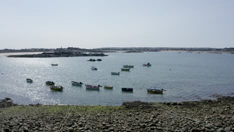 low drone footage over calm natural harbour, low sunlight reflecting off sea with fishing boats at anchor, foreshore and mooring lines,small island in background