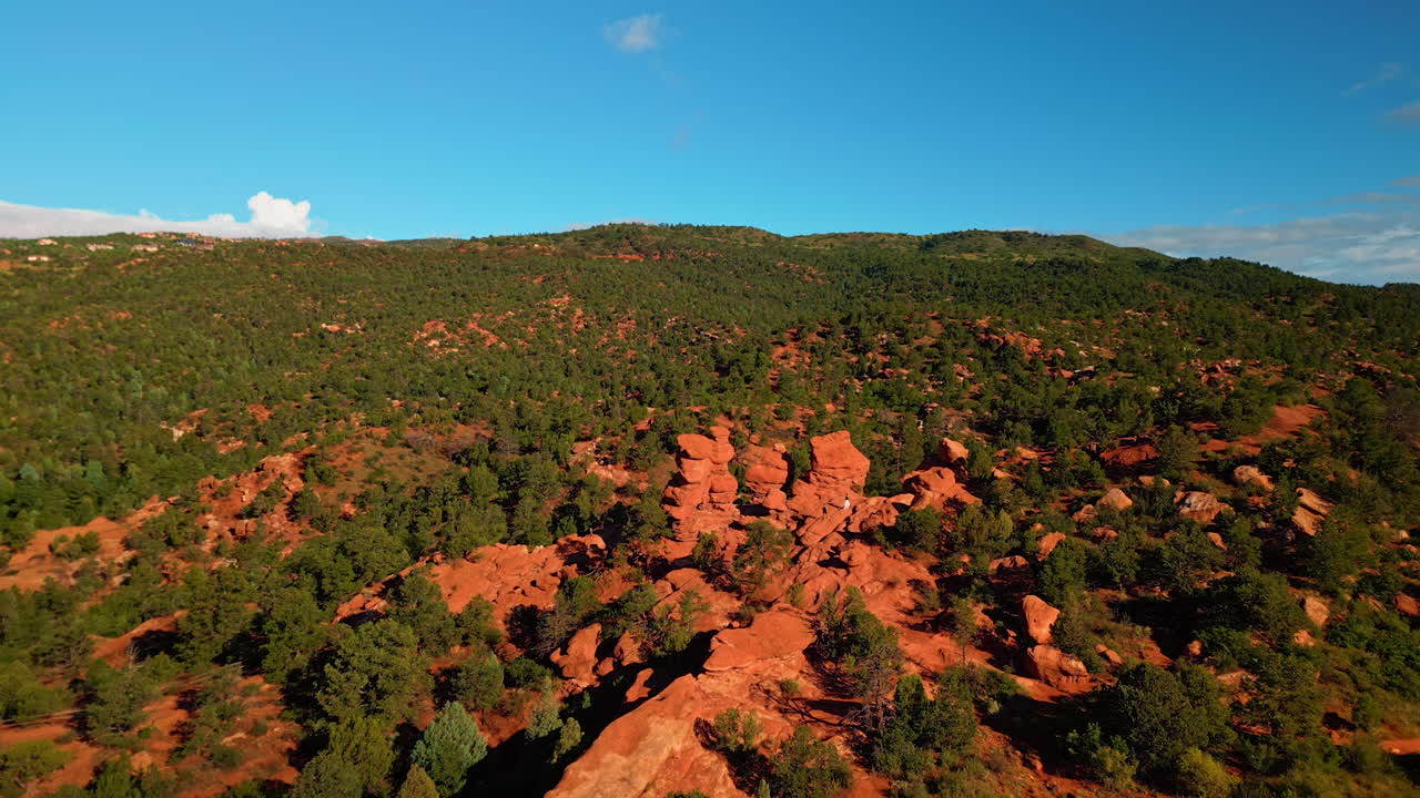 Flying away from a couple taking pictures in the red rock formations in the Garden of the Gods Park, Colorado Springs, Colorado, USA. Revealing view on the rocky landscape covered with trees and bushes