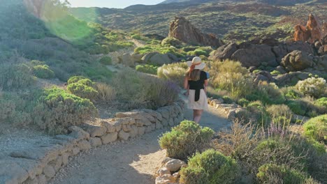 Una-Madre-Cargando-A-Su-Hijo-Caminando-Por-El-Sendero-Del-Parque-Nacional-Del-Teide-Con-Fondo-Montañoso,-Dinámico