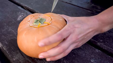 hands cutting off the lid of a pumpkin, preparing evil pumpkin for halloween