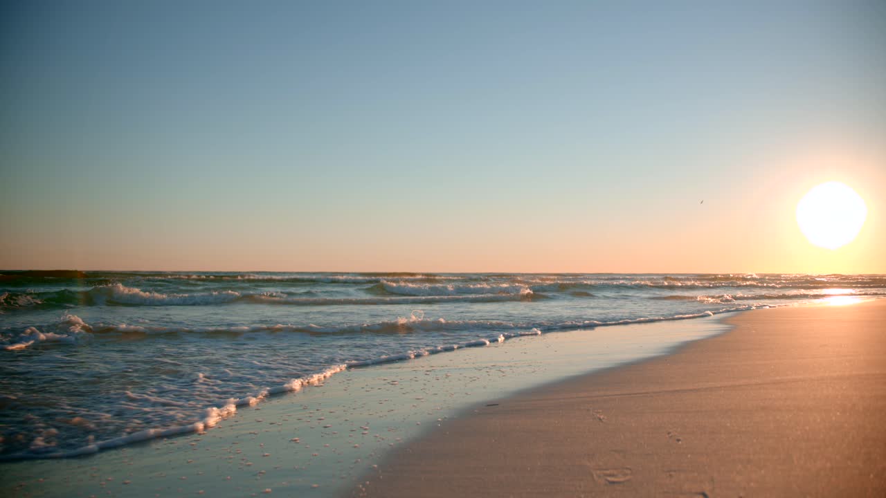 Shots of the ocean on a warm, sunny evening with footprints in the sand facing the sun directly