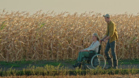 man pushing woman in wheelchair through a cornfield