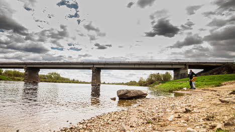 timelapse shot of a fishing family busy fishing along the riverside on the cloudy day with the view of a bridge in the background