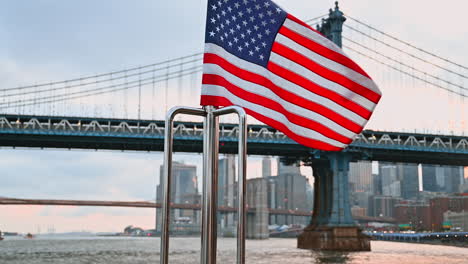 flapping flag of america on the front of the boat. famous manhattan bridge and new york skyline at backdrop