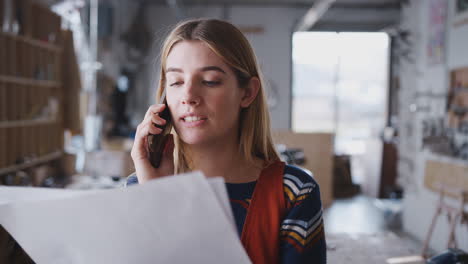 Female-Business-Owner-In-Workshop-For-Building-Bicycles-Making-Call-On-Mobile-Phone