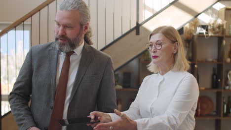 senior male and female colleagues walking with tablet and speaking