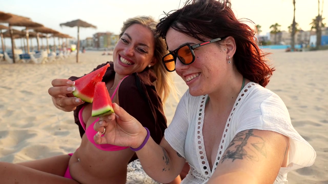 Due donne felici che mangiano anguria in spiaggia al tramonto