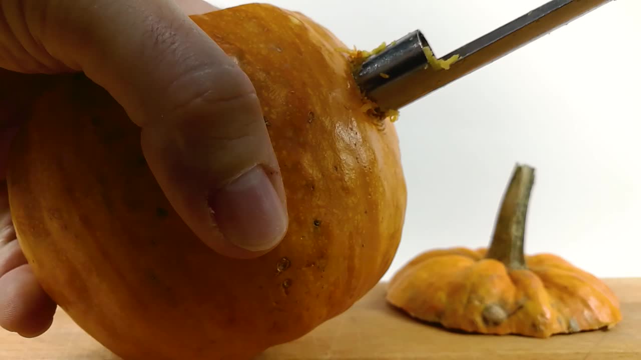 Carving pumpkin part 3, Person carving eye into Halloween pumpkin with a small  serrated apple corer knife on wooden chopping board, STILL, ISOLATED