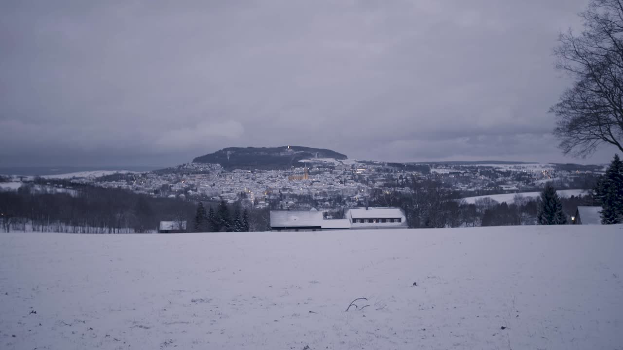 Snow-covered town at dusk with distant hills and cloudy sky