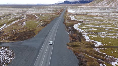 un dron aéreo sigue a un coche blanco, conduciendo a través de las montañas nevadas volcánicas de islandia.