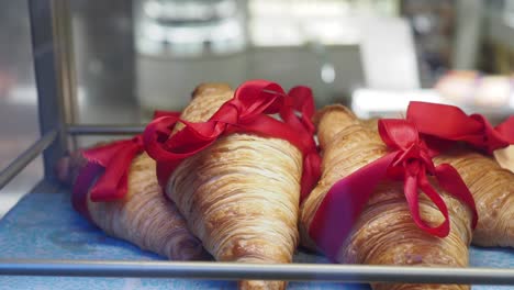 close-up of croissants with red ribbons in a bakery display case